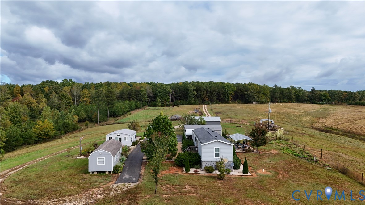Expansive acreage featuring a paved driveway, multiple detached structures, a metal-roofed residence, and extensive open pasture land bordered by mature trees