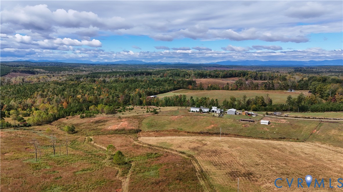 Expansive acreage featuring rolling open fields, scattered mature trees, multiple outbuildings, and distant mountain horizons