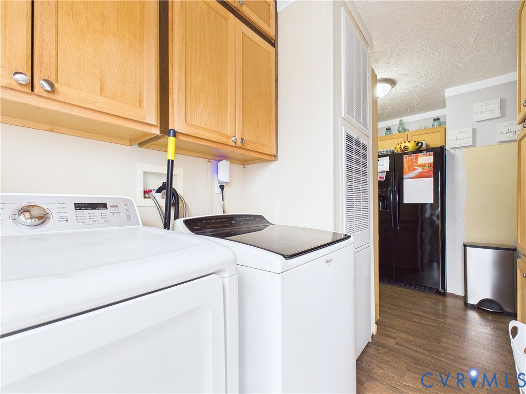 Laundry space featuring upper wood cabinetry, wood-finish flooring, and a built-in black refrigerator