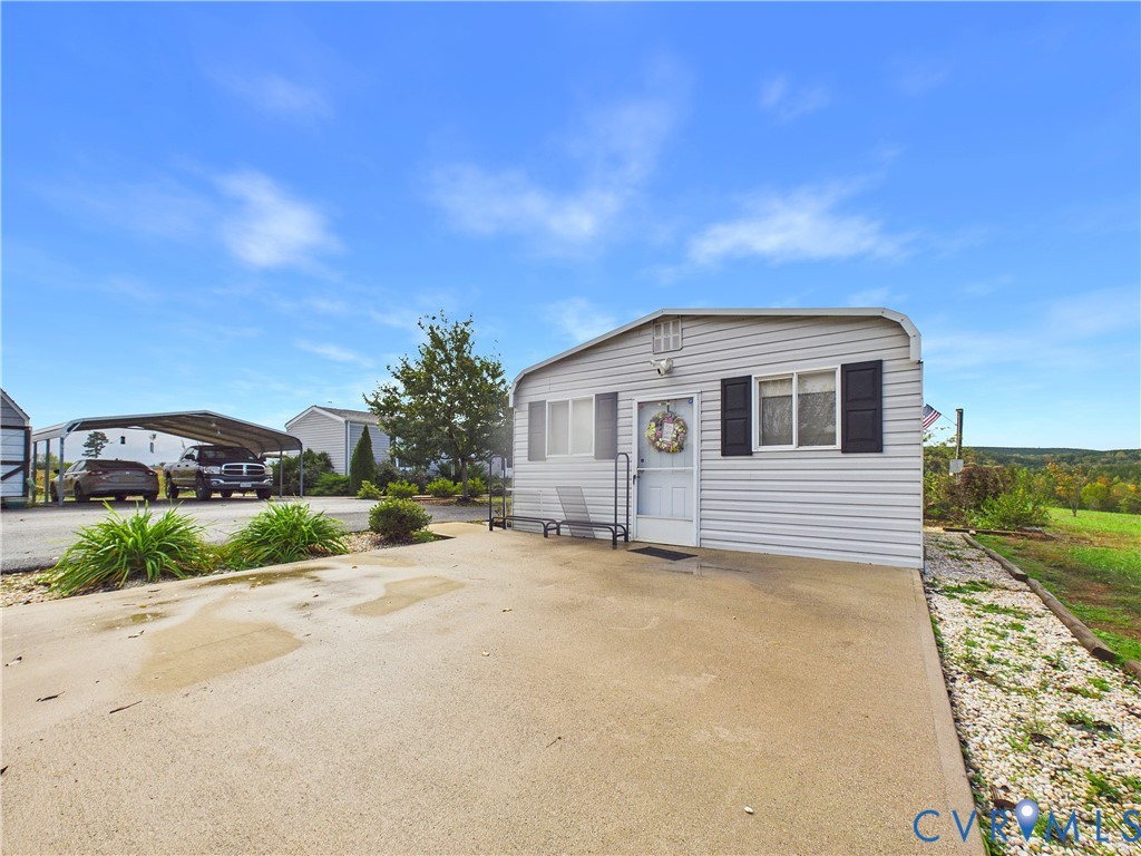 Exterior featuring light gray horizontal siding, dark decorative shutters, a concrete parking pad, and an attached metal-framed carport
