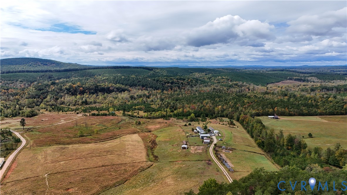 Aerial perspective of expansive acreage featuring open pasture, mature woodland, natural topography, and a private gravel drive