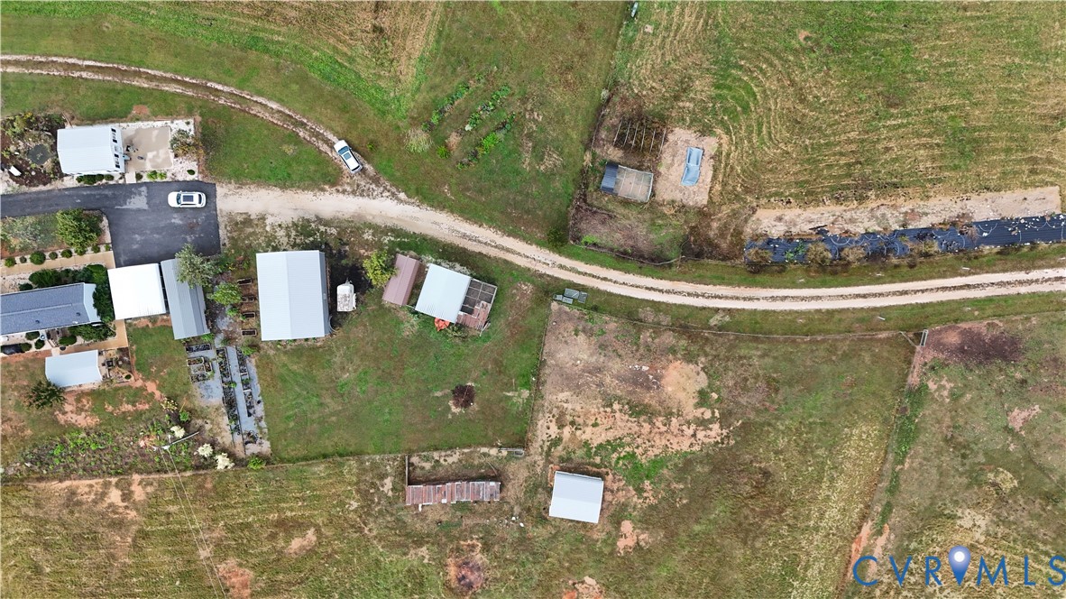 Aerial perspective of rural acreage featuring multiple outbuildings, open pasture land, and a gravel access road