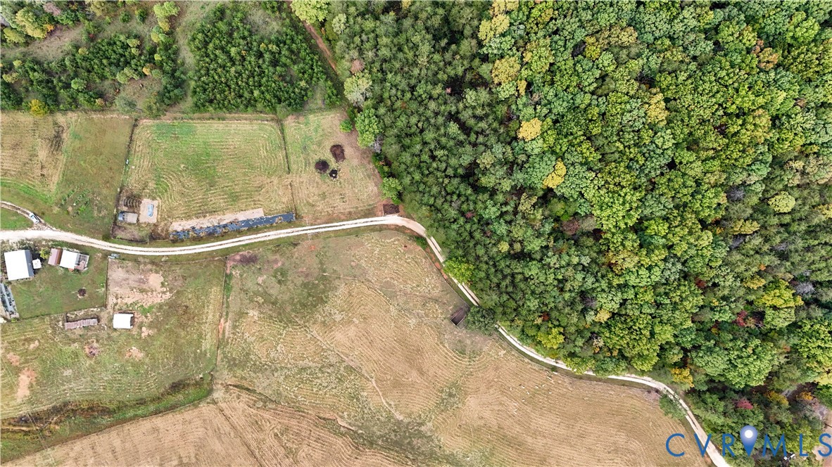 Aerial perspective featuring expansive acreage, mature forest borders, cleared pastureland, and winding gravel thoroughfares