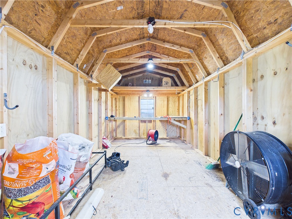 Storage structure featuring exposed wood framing, plywood wall paneling, a gambrel roof design, built-in shelving, and a single window