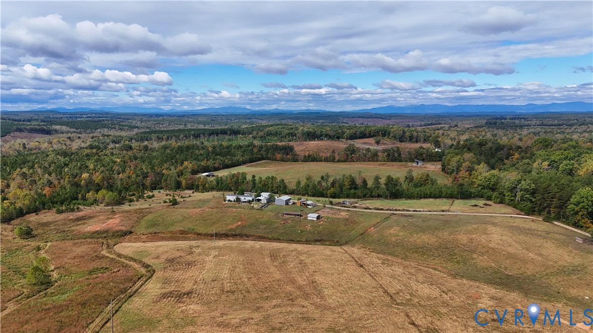 Expansive acreage featuring rolling meadows, multi-structure site, unpaved access paths, and mountain backdrop