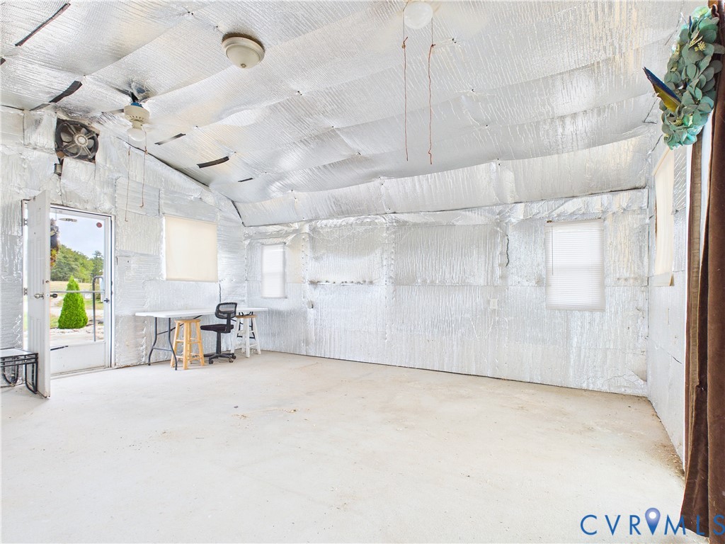 Interior space featuring concrete flooring, reflective metallic-finish wall and ceiling insulation, three windows, and an installed wall-mounted ventilation fan