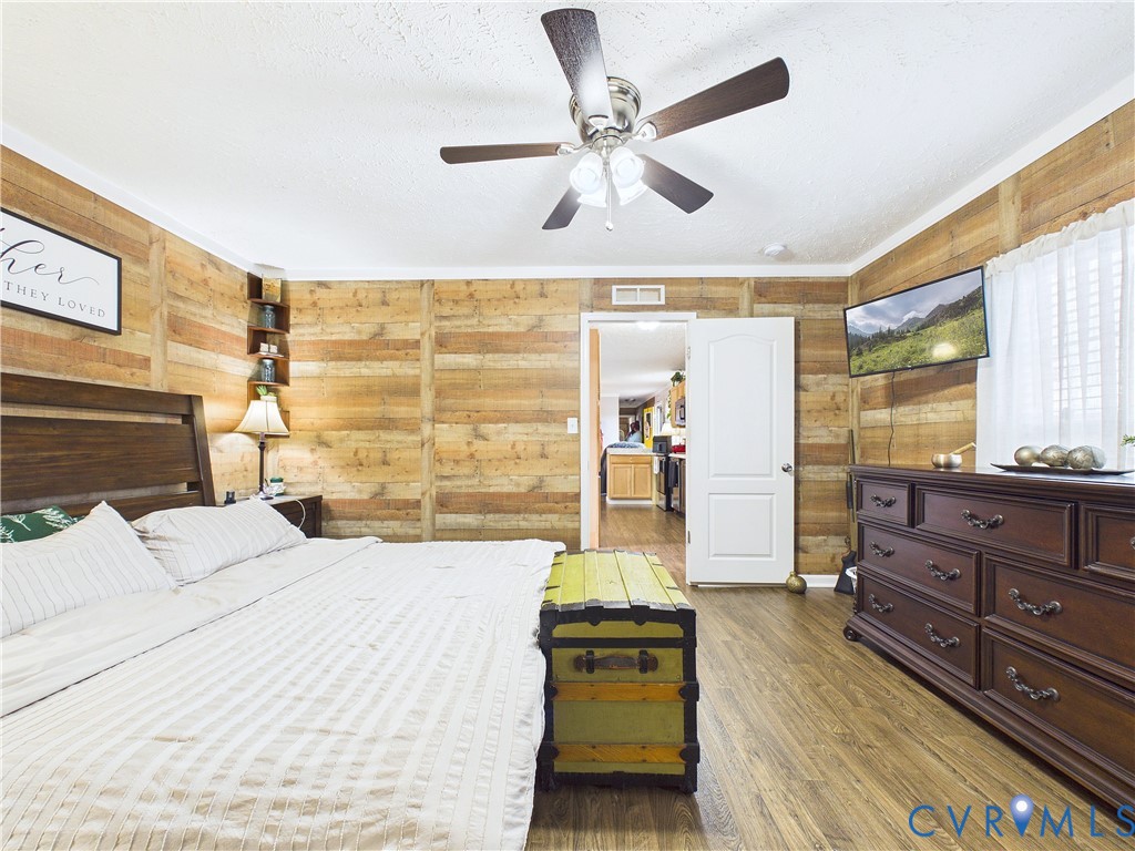 Interior room featuring horizontal wood-plank wall paneling, wood-finish flooring, a centrally mounted ceiling fan with integrated light fixture, and a white six-panel door