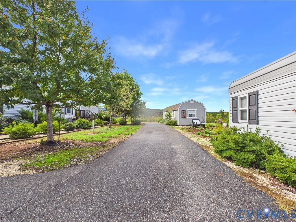 Asphalt driveway featuring a detached storage shed, exterior siding, mature trees, and landscaped shrubbery Asphalt driveway featuring a detached storage shed, exterior siding, mature trees, and landscaped shrubbery