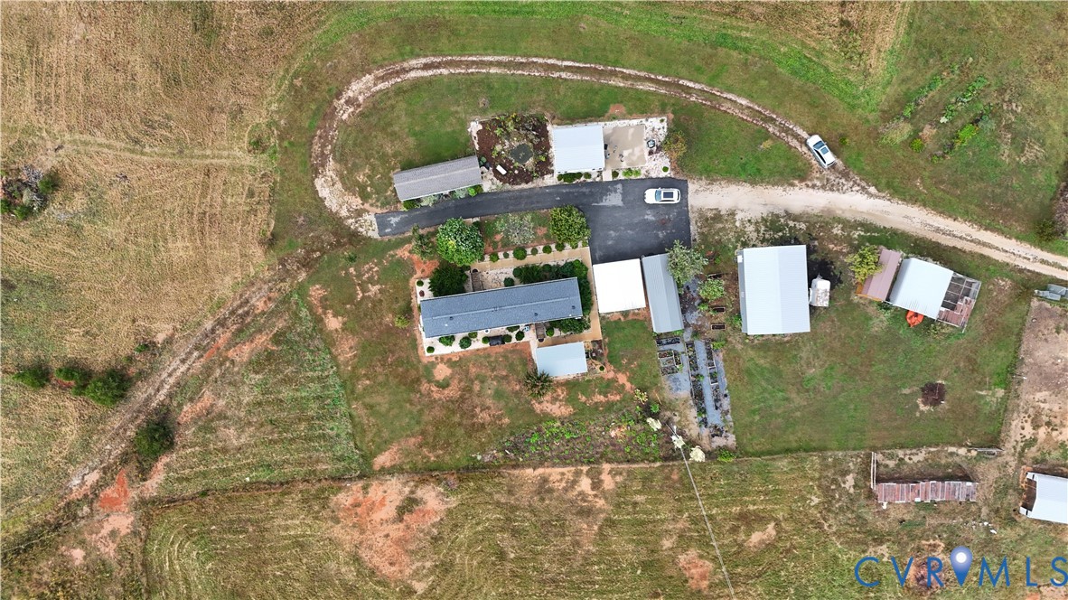 Aerial perspective of a sprawling property featuring multiple detached outbuildings, expansive pastureland, a paved driveway, and established landscaping