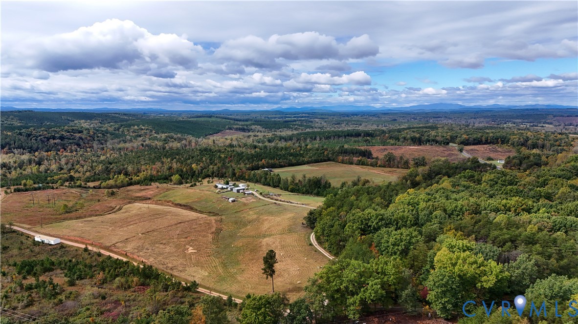 Expansive acreage featuring cleared pasture, dense woodlands, a private gravel road, and distant mountain topography