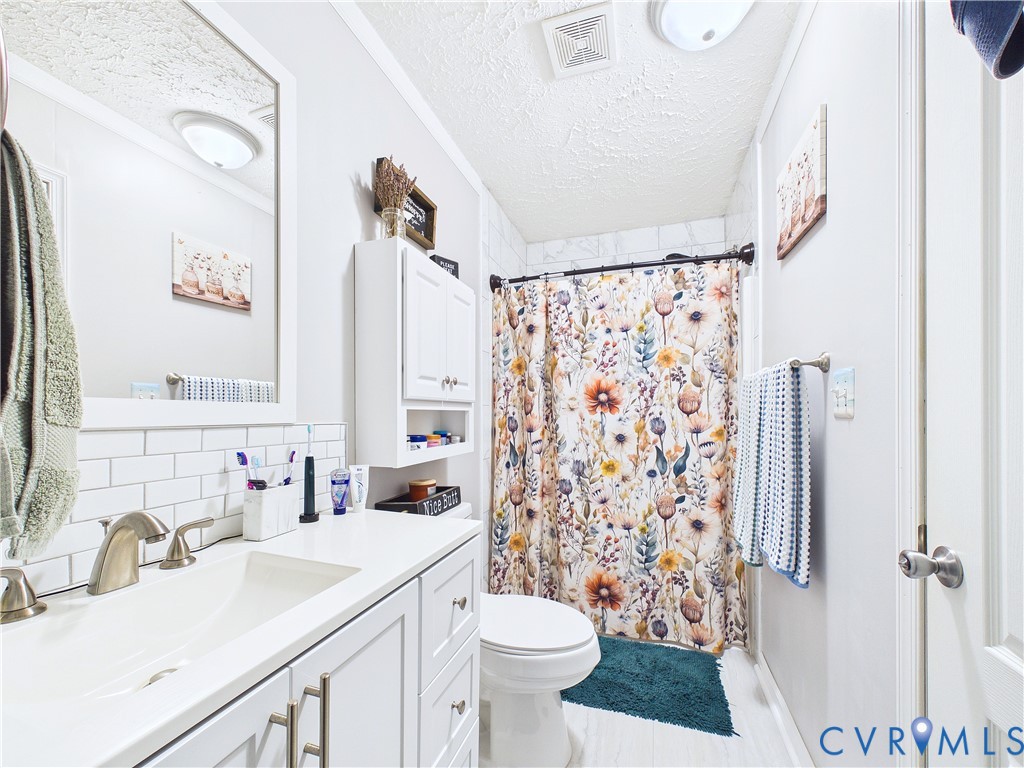 Bathroom featuring a white vanity cabinet with a solid-surface countertop, rectangular undermount sink, classic subway tile backsplash, and a wall-mounted storage cabinet