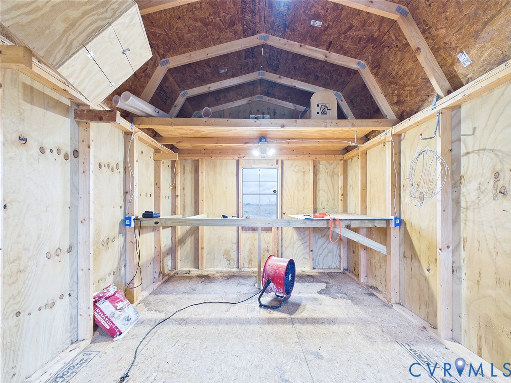Outbuilding featuring exposed wood stud framing, plywood paneling, an elevated storage loft, and a built-in workbench