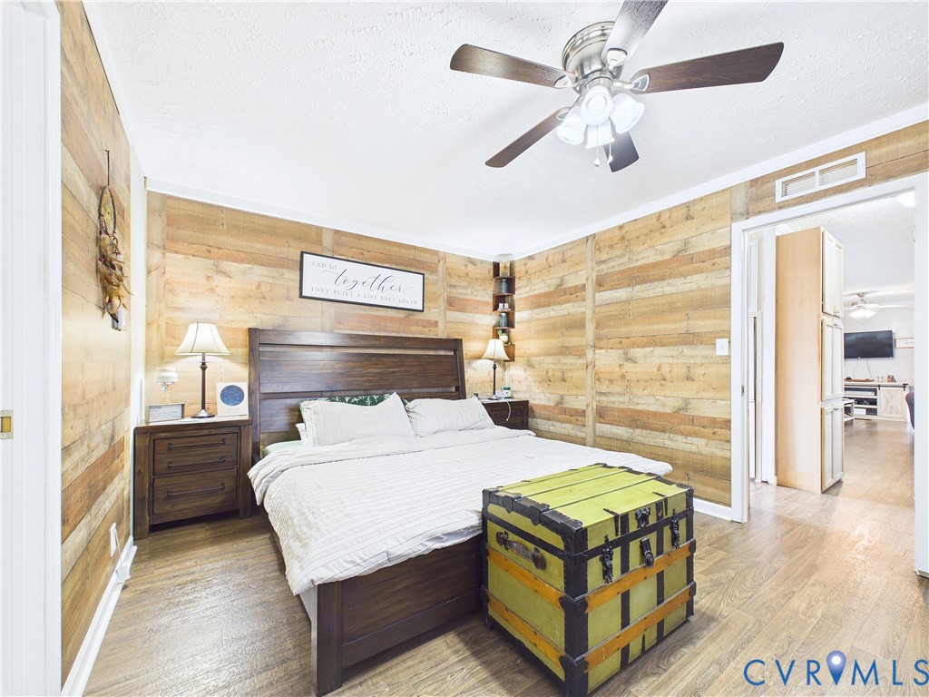 Room featuring horizontal wood plank wall paneling, wood-finish flooring, and a ceiling fan with integrated lighting