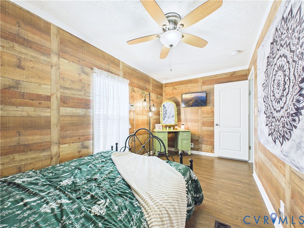 Wood-plank wall paneling, wood-finish flooring, and a multi-blade ceiling fan with an integrated light fixture