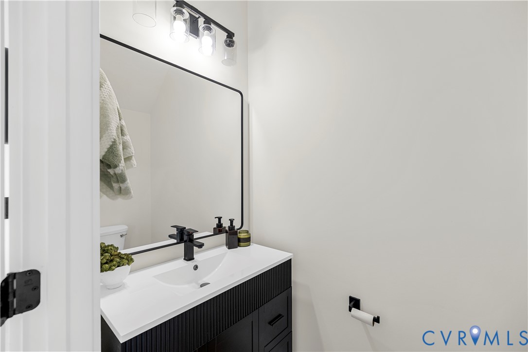 Black fluted vanity with a white countertop, rectangular integrated sink, matte black widespread faucet, and matching black-framed wall mirror with a multi-light fixture