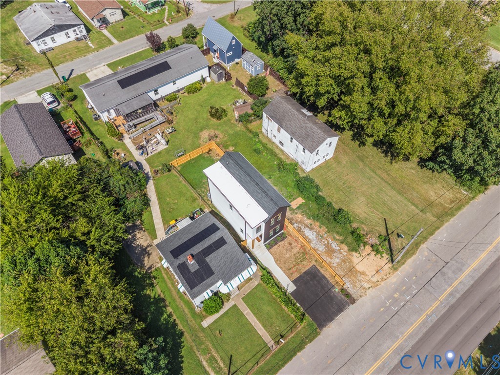 Aerial perspective featuring a multi-level structure with a metal roof, solar panel array, paved driveway, wood-fencing, and expansive lawn area