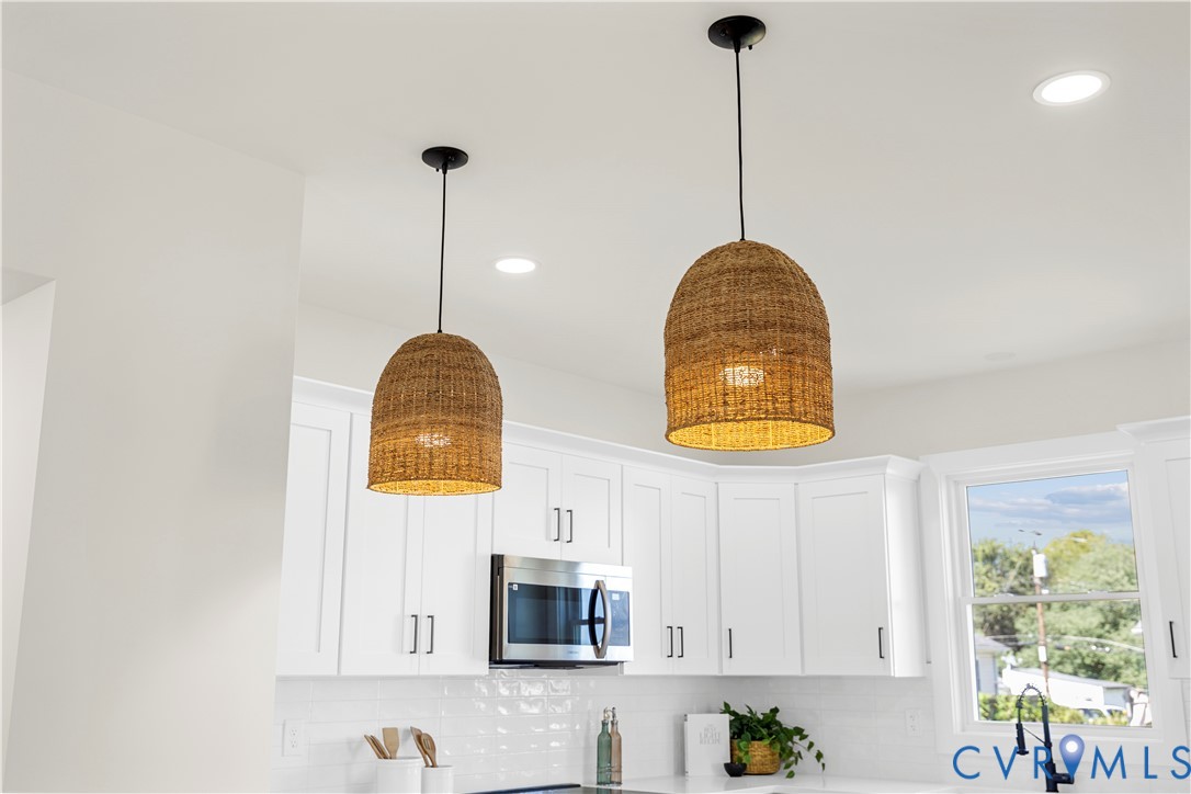 White Shaker-style cabinetry, stainless steel microwave, woven dome pendant lighting, white subway tile backsplash, and matte black faucet