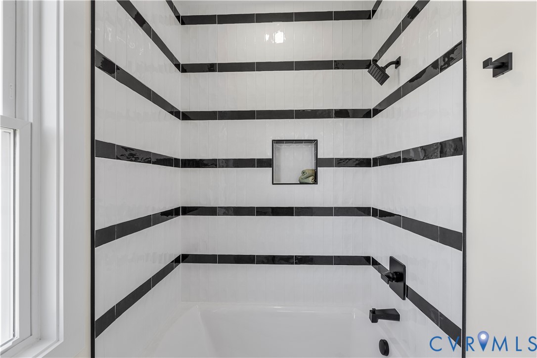 Shower featuring white subway tile walls with horizontal black accent stripes, integrated square tile niche, and matte black fixtures