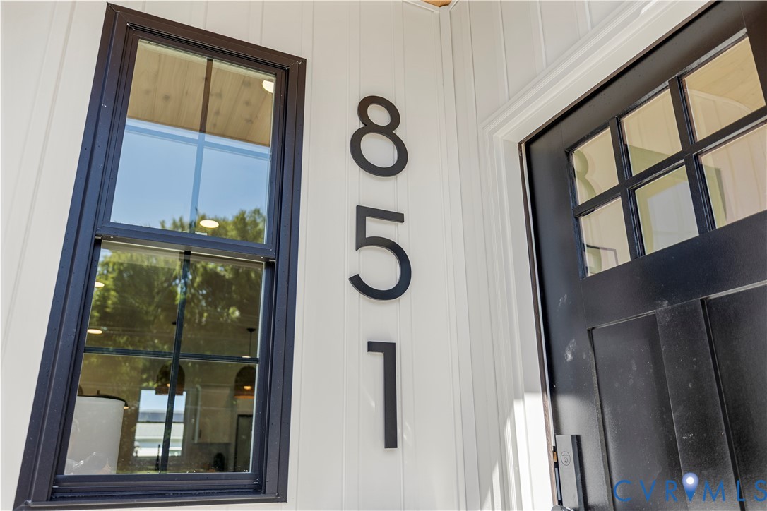 White vertical siding exterior featuring a black entry door with multi-pane glass inserts, dark-framed window, and matte black oversized house numbers