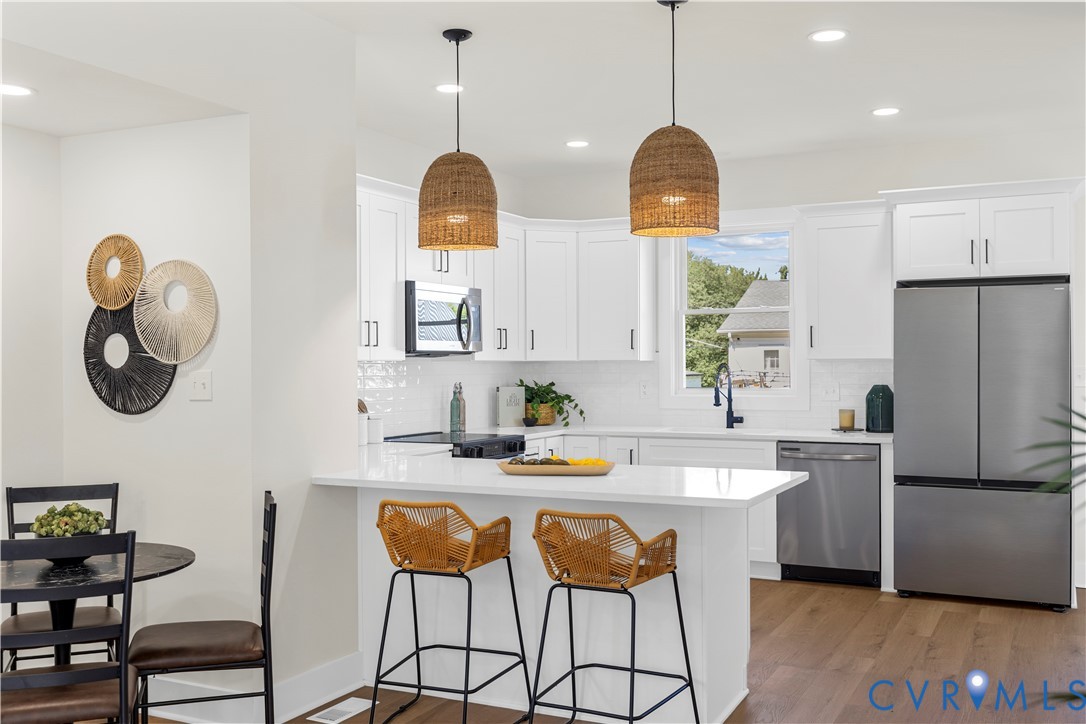 Kitchen featuring white shaker-style cabinetry, a solid-surface breakfast bar, stainless steel appliances, woven pendant lighting, and wood-finish flooring