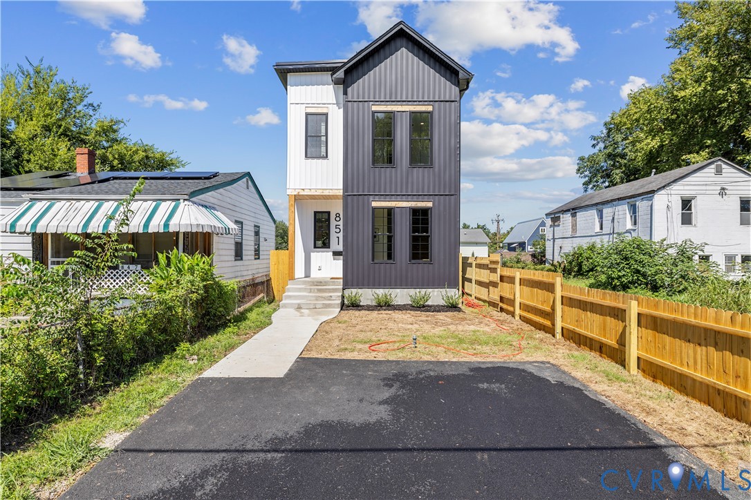 Two-story residence featuring vertical metal panel siding, a covered entryway with concrete steps, and a private asphalt driveway