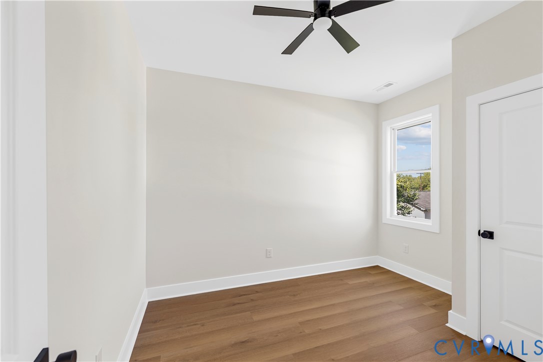 Room featuring wood-finish flooring, neutral wall paint, a multi-blade ceiling fan, and a paneled interior door with matte black hardware