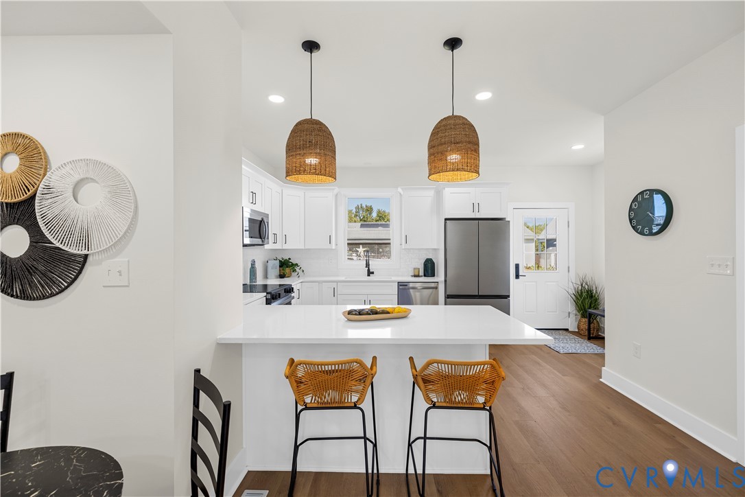 Kitchen featuring white cabinetry, solid-surface countertops, wood-finish flooring, two woven pendant lights, and stainless steel appliances Kitchen featuring white cabinetry, solid-surface countertops, wood-finish flooring, two woven pendant lights, and stainless steel appliances