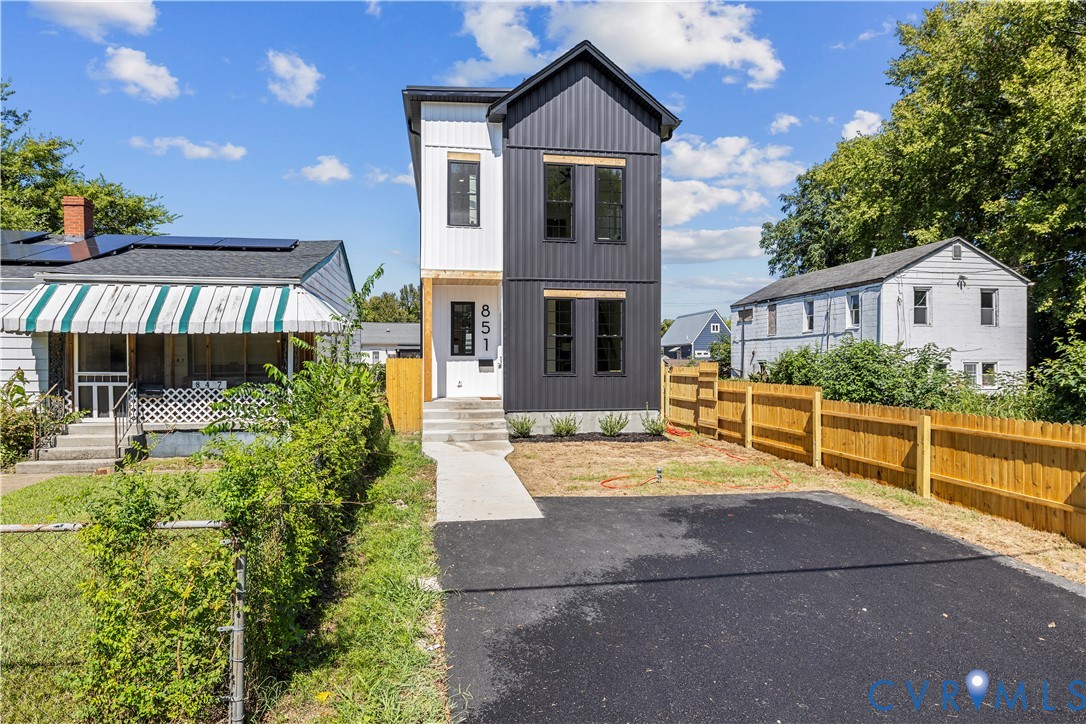 Modern two-story exterior featuring vertical metal siding, high-contrast black and white color palette, concrete entryway steps, and an asphalt driveway