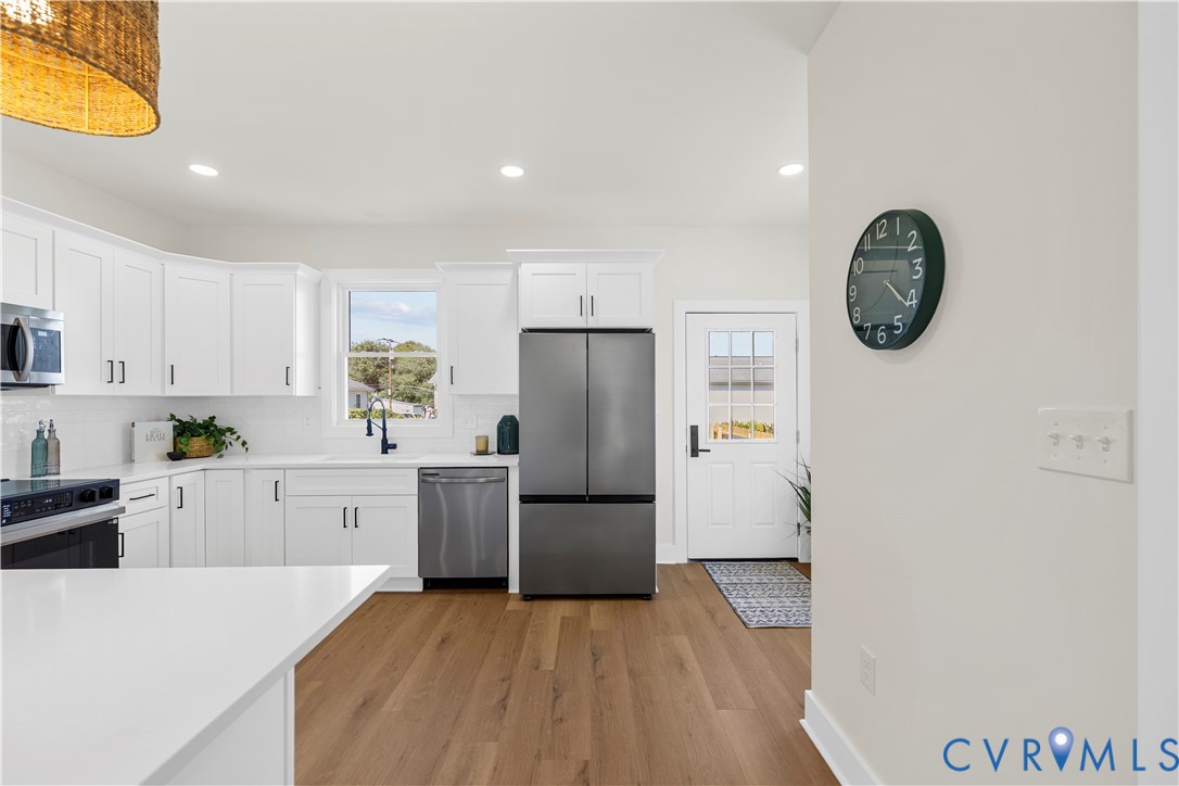 Kitchen featuring white cabinetry, wood-finish flooring, stainless steel appliances, quartz countertops, and a single-light glass panel exterior door