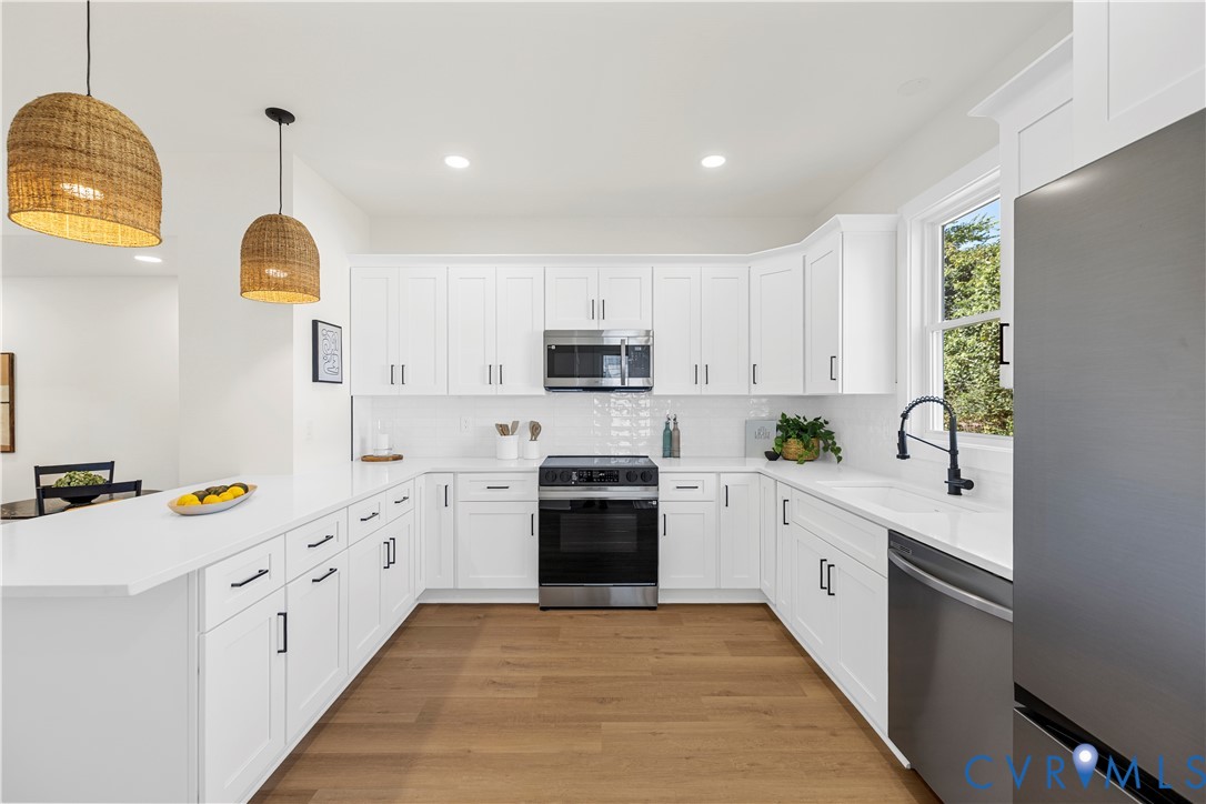 Kitchen featuring white shaker-style cabinetry, quartz countertops, subway tile backsplash, stainless steel appliances, and wood-finish flooring Kitchen featuring white shaker-style cabinetry, quartz countertops, subway tile backsplash, stainless steel appliances, and wood-finish flooring