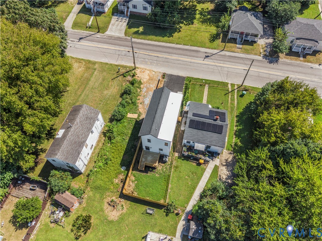 Aerial view of a residential lot featuring a multi-level deck, fenced rear yard, solar panel installation, asphalt driveway, and mature landscaping