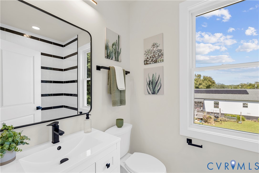 White vanity with a rectangular sink, matte black faucet, wall-mounted mirror with a black frame, and shower enclosure featuring horizontal black and white tile accents