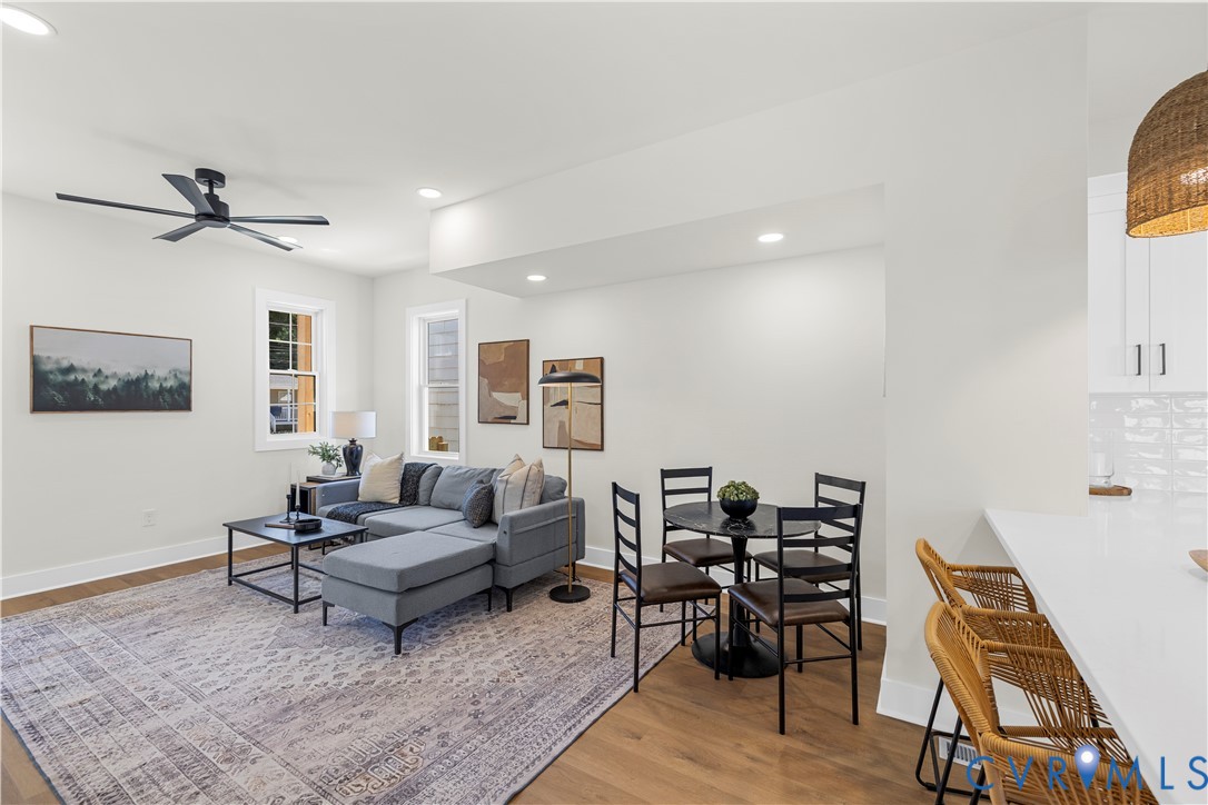 Open-concept space featuring wood-finish flooring, a matte black ceiling fan, recessed lighting, and a kitchen peninsula with a solid-surface countertop Open-concept space featuring wood-finish flooring, a matte black ceiling fan, recessed lighting, and a kitchen peninsula with a solid-surface countertop