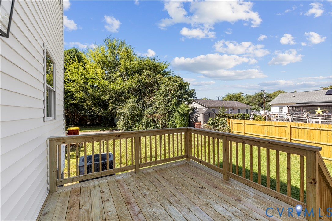 Elevated wood deck featuring vertical baluster railings, wood plank flooring, and stairs, overlooking a fenced backyard
