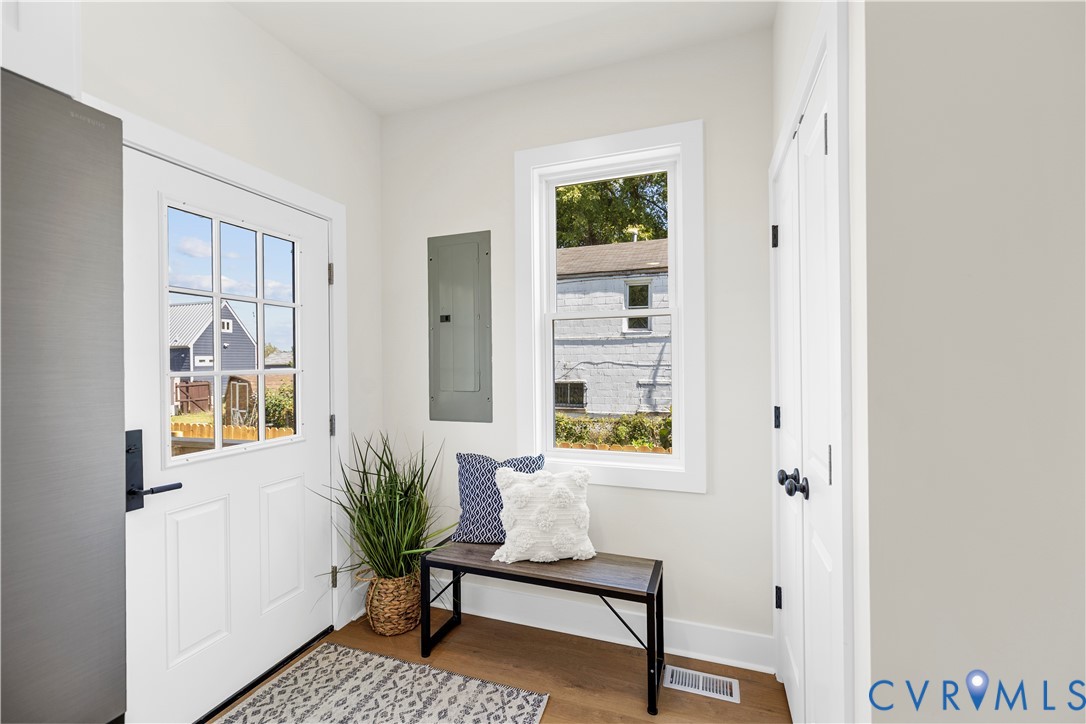 Entryway featuring wood-finish flooring, a six-pane glass window door, a single-pane vertical window, and dual-panel closet doors with matte black hardware