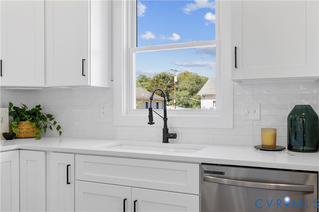 Kitchen featuring white shaker-style cabinetry, solid-surface countertops, horizontal subway tile backsplash, farmhouse-style apron sink with a matte black pull-down faucet, and stainless steel dishwasher Kitchen featuring white shaker-style cabinetry, solid-surface countertops, horizontal subway tile backsplash, farmhouse-style apron sink with a matte black pull-down faucet, and stainless steel dishwasher