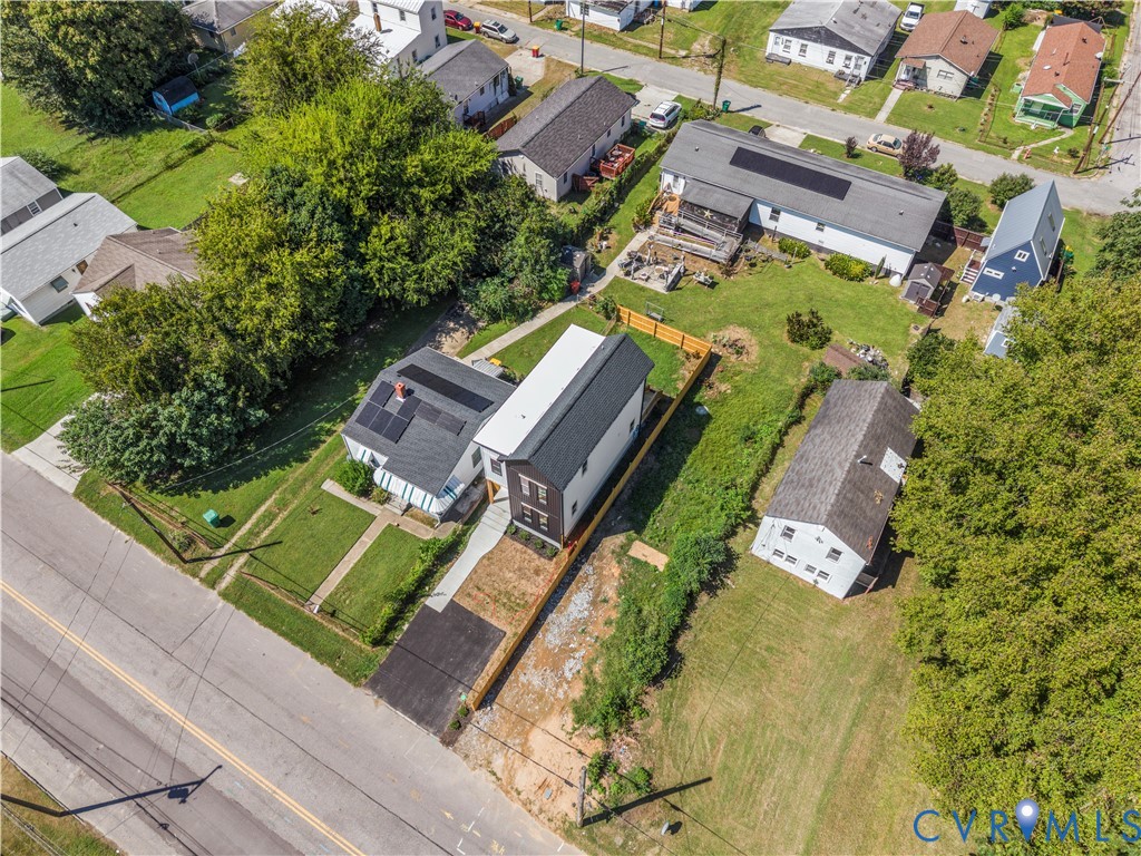 Aerial perspective featuring a two-story residence with a dark metal roof, solar panel installation, asphalt driveway, and wood-style perimeter fencing