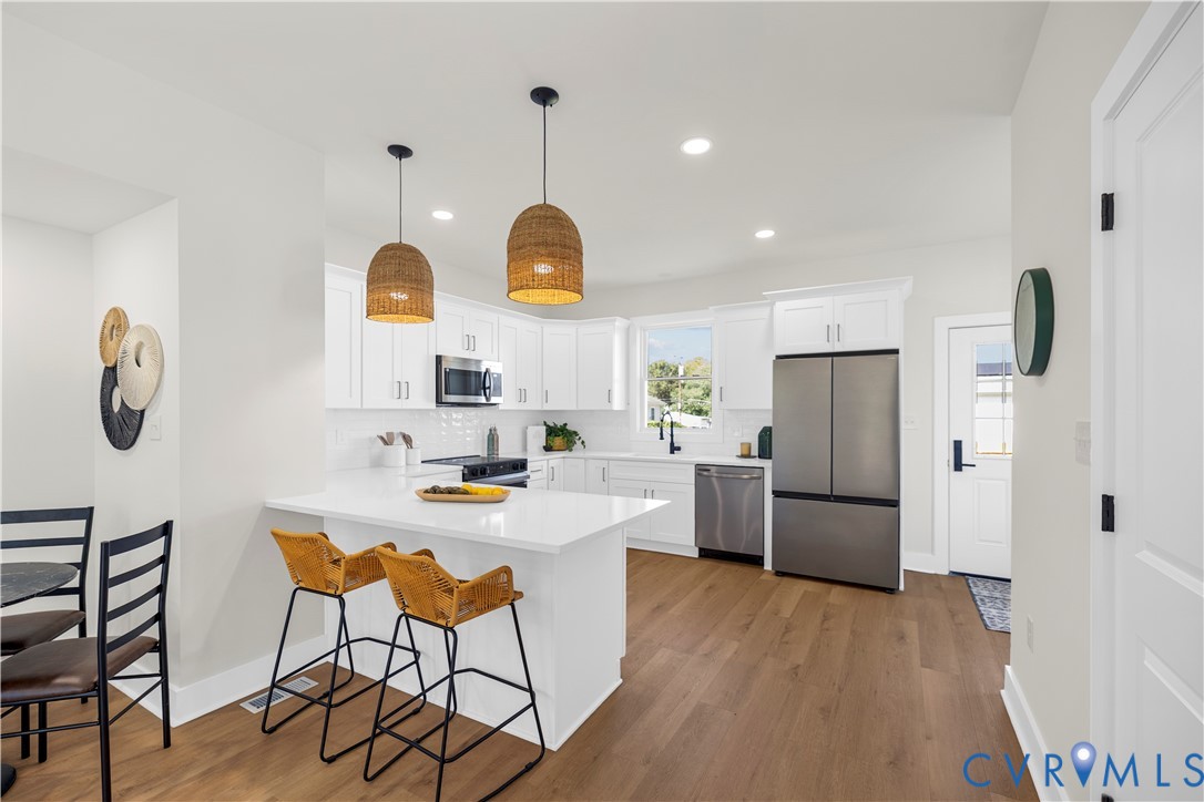 Kitchen featuring white cabinetry, quartz countertops, wood-finish flooring, stainless steel appliances, and woven pendant lighting