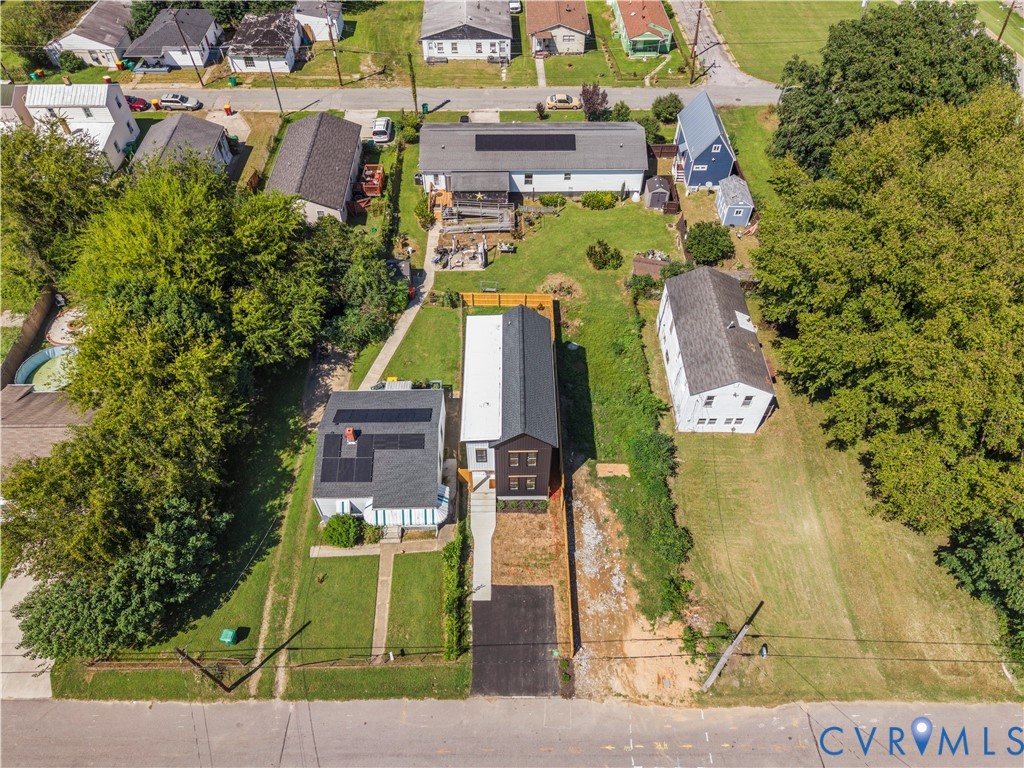 Aerial view featuring a two-story residence with a dark metal roof, solar panels, a paved driveway, and a wood privacy fence