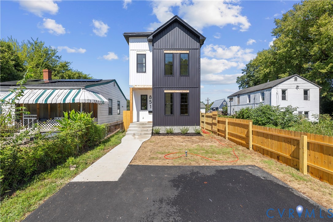 Two-story architectural exterior featuring vertical panel siding, dark-toned metal cladding, a concrete front walkway, and a paved driveway Two-story architectural exterior featuring vertical panel siding, dark-toned metal cladding, a concrete front walkway, and a paved driveway