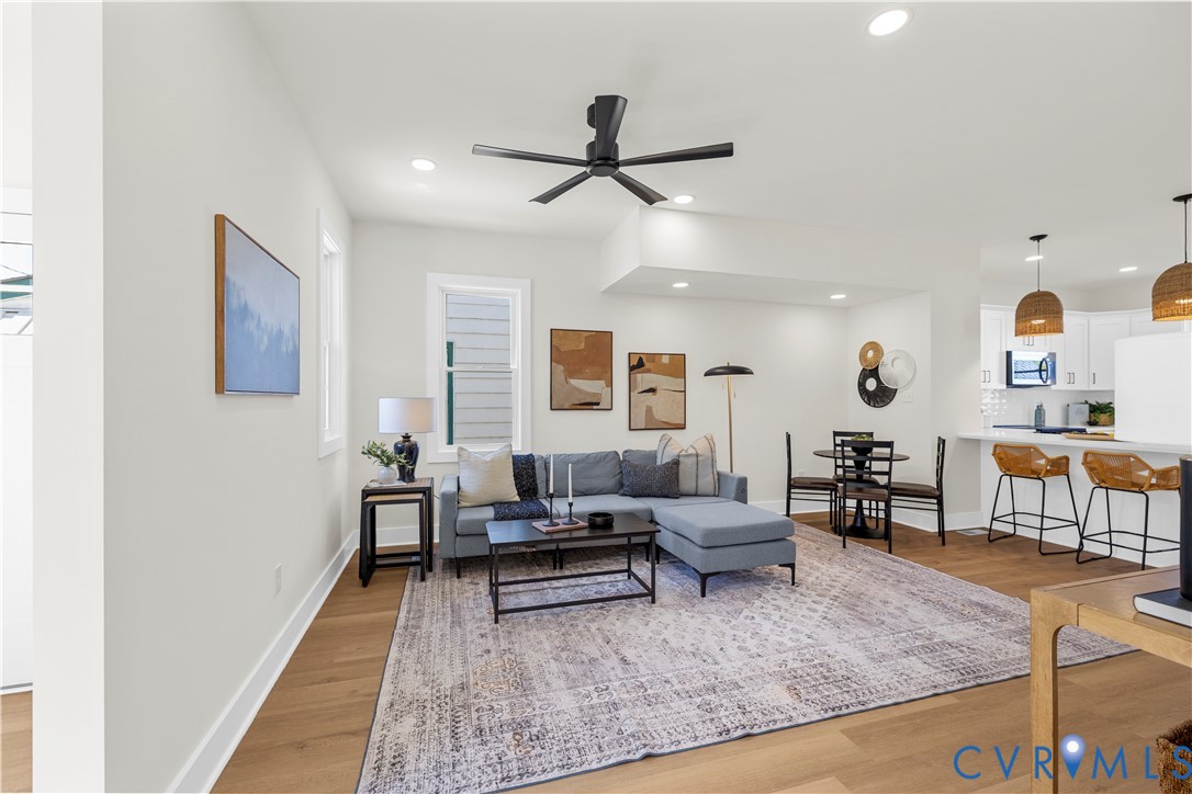Open-concept interior featuring wood-finish flooring, recessed lighting, a modern matte black ceiling fan, and a breakfast bar with dual pendant lighting Open-concept interior featuring wood-finish flooring, recessed lighting, a modern matte black ceiling fan, and a breakfast bar with dual pendant lighting