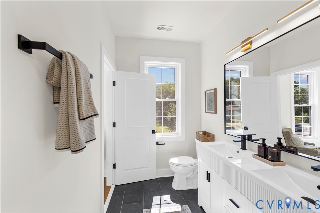 Bathroom featuring a white dual-sink vanity with fluted cabinetry, large rectangular mirrors, matte black fixtures, and dark-toned floor tiling