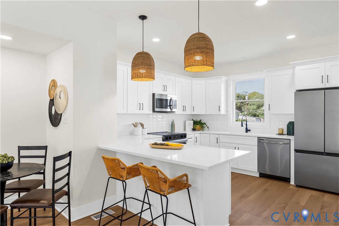 Kitchen featuring white cabinetry, solid-surface countertops, stainless steel appliances, wood-finish flooring, and woven pendant lighting Kitchen featuring white cabinetry, solid-surface countertops, stainless steel appliances, wood-finish flooring, and woven pendant lighting