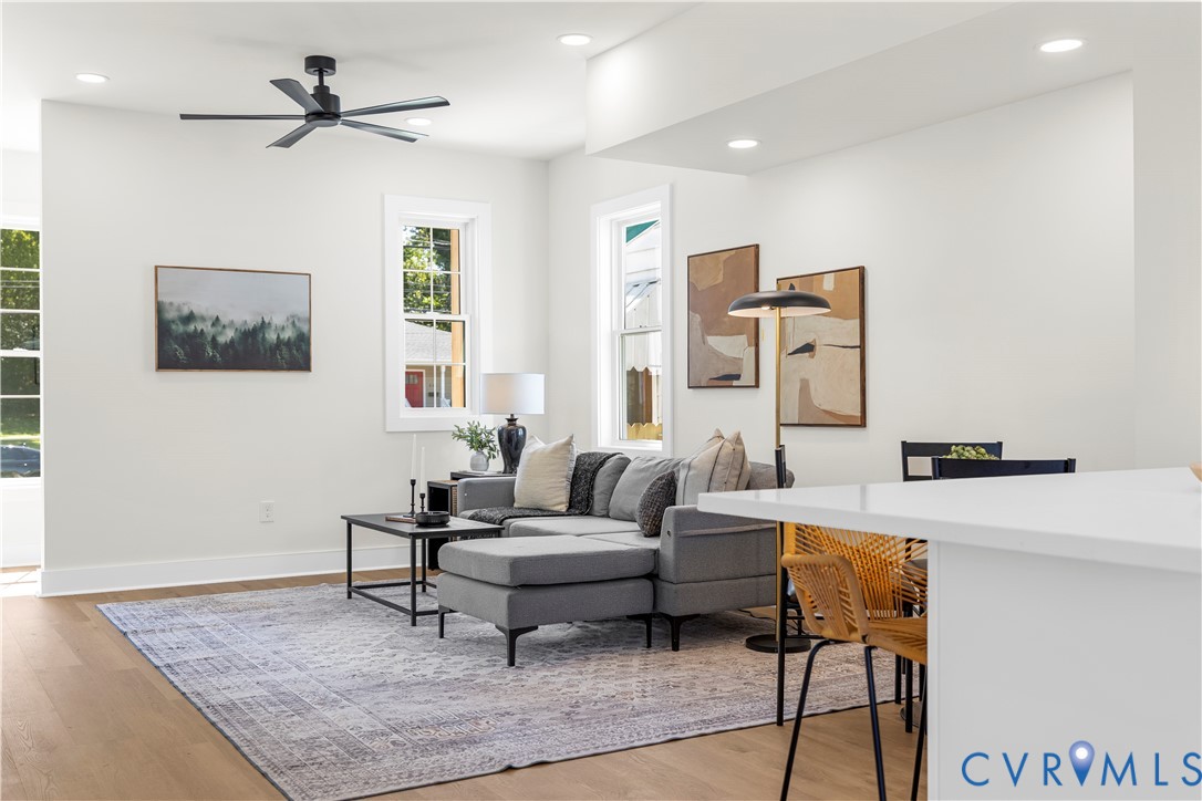 Open floor plan featuring wood-finish flooring, recessed lighting, matte black ceiling fan, and large windows with white trim
