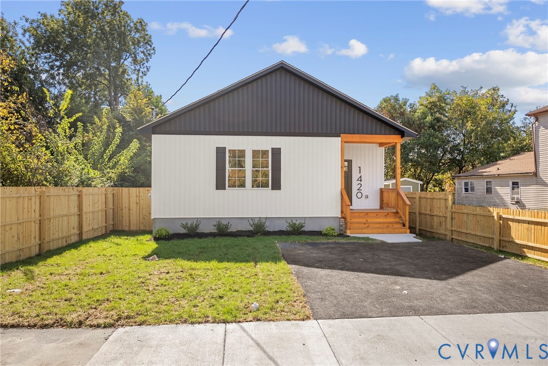 Single-story residence featuring vertical siding, metal roof gable, wood-framed front porch, asphalt driveway, and enclosed perimeter fencing