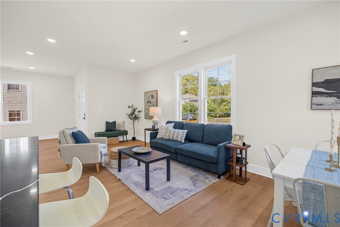 Open-concept interior featuring light wood-finish flooring, recessed lighting, and large double-pane windows