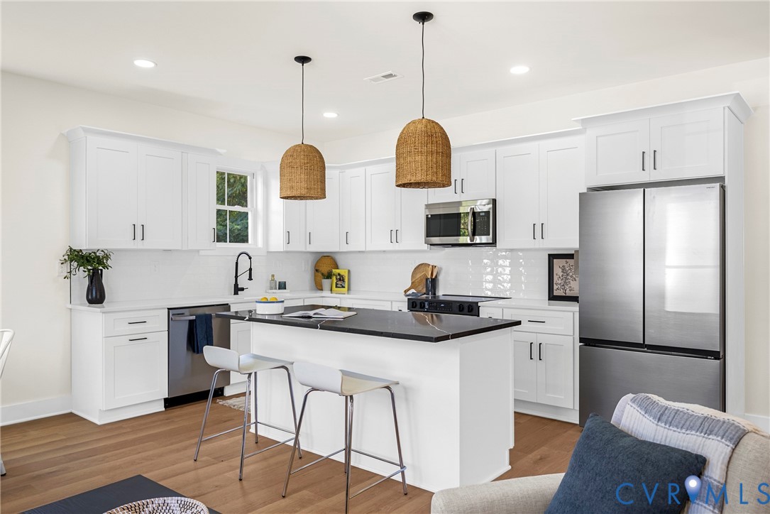 Kitchen featuring white shaker-style cabinetry, center island with dark stone countertop, stainless steel appliances, white subway tile backsplash, and wood-finish flooring Kitchen featuring white shaker-style cabinetry, center island with dark stone countertop, stainless steel appliances, white subway tile backsplash, and wood-finish flooring