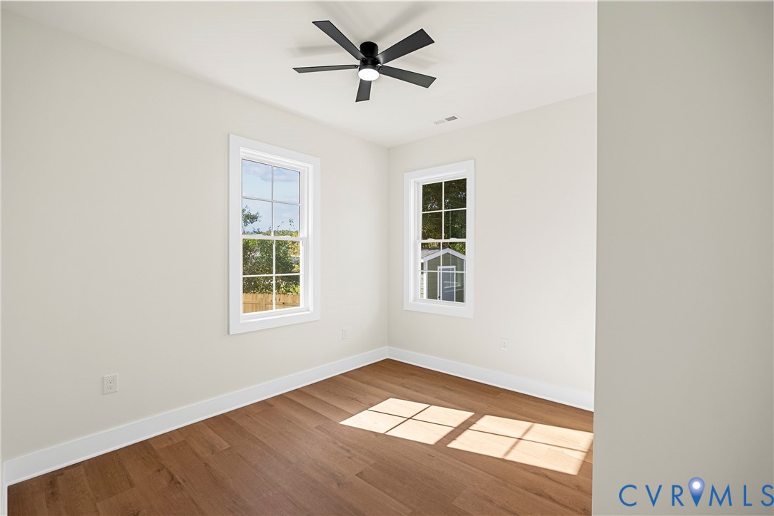 Room featuring wood-finish flooring, two double-hung windows with grid detailing, and a black ceiling-mounted fan with integrated lighting