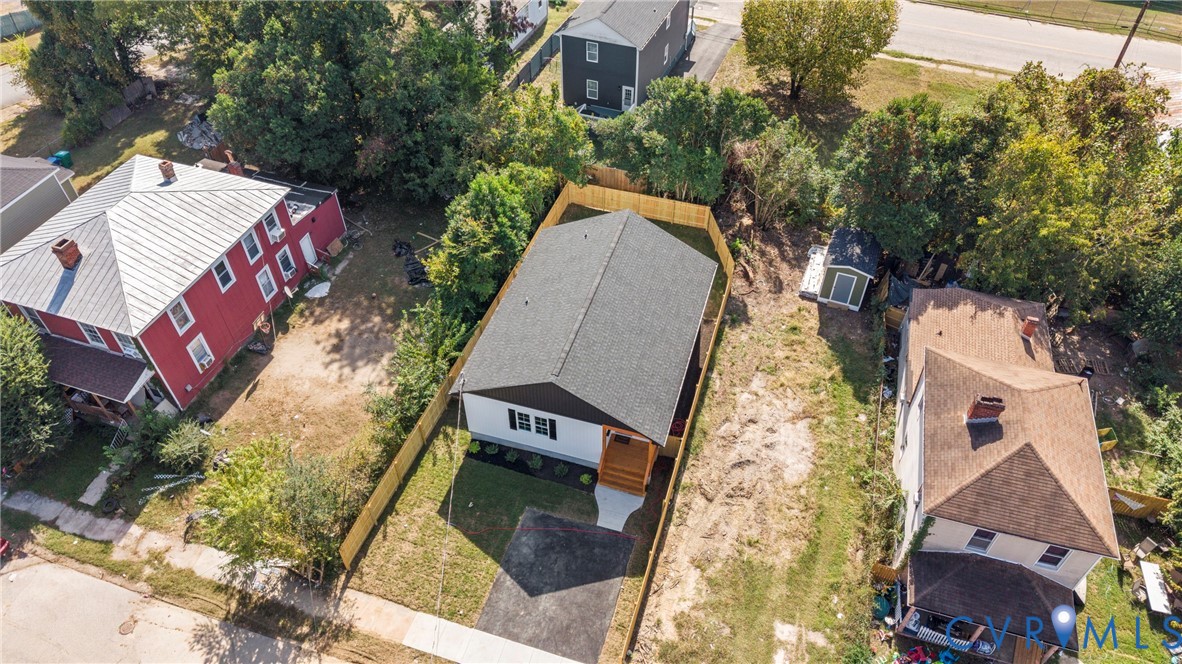 Aerial view of a residential lot featuring a detached house, asphalt driveway, fenced yard, and an external storage structure