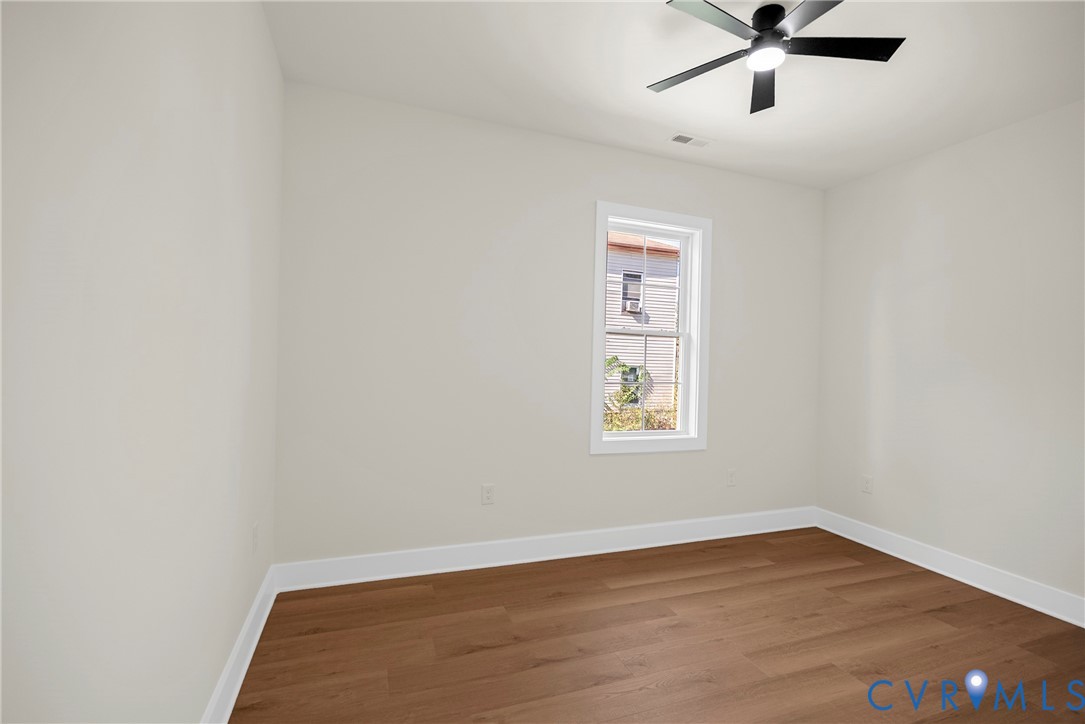 Neutral interior space featuring wood-finish flooring, a single-hung window with white casing, and a matte black ceiling fan with an integrated light fixture